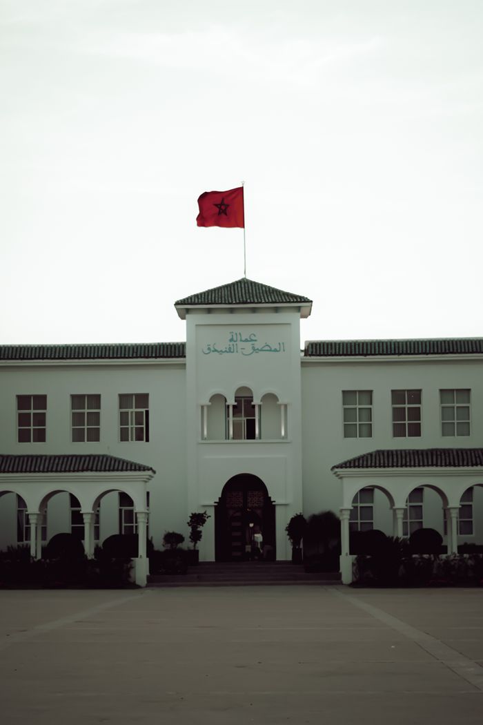 service-04 A Moroccan governmental building adorned with the national flag highlighting its architectural style.