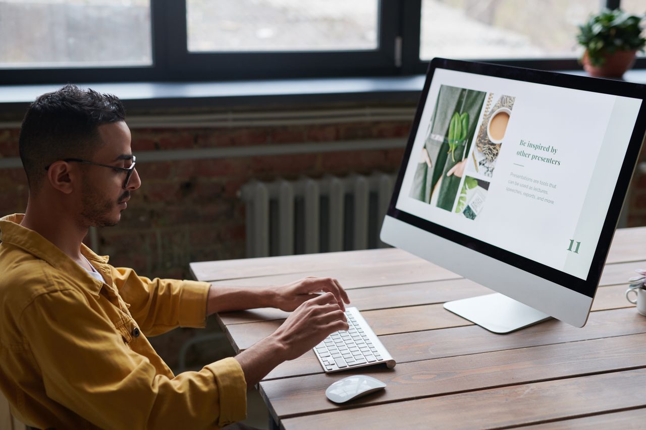Mastering the First Impression: Your intriguing post title goes here A young man in casual wear works on a computer at a wooden table in a modern, stylish office.